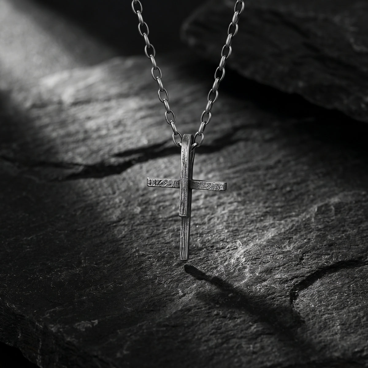 Front view of the textured silver cross pendant hanging from its chain over dark slate.
