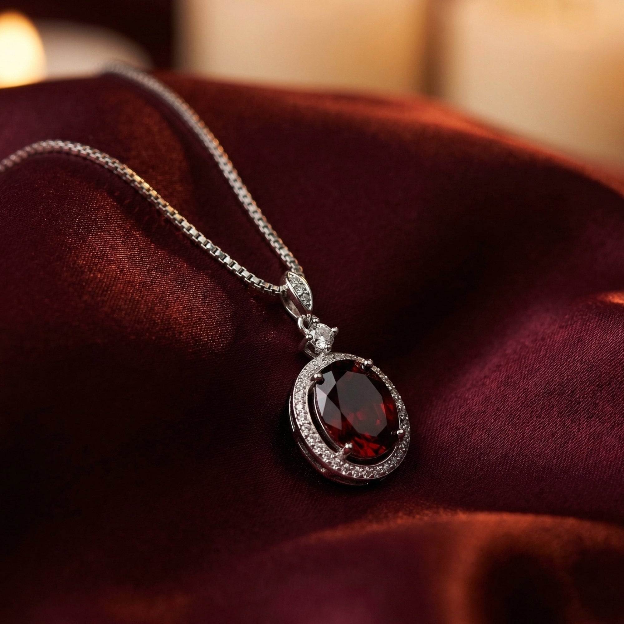 Macro view of the oval-cut garnet pendant and sterling silver box chain on textured fabric.