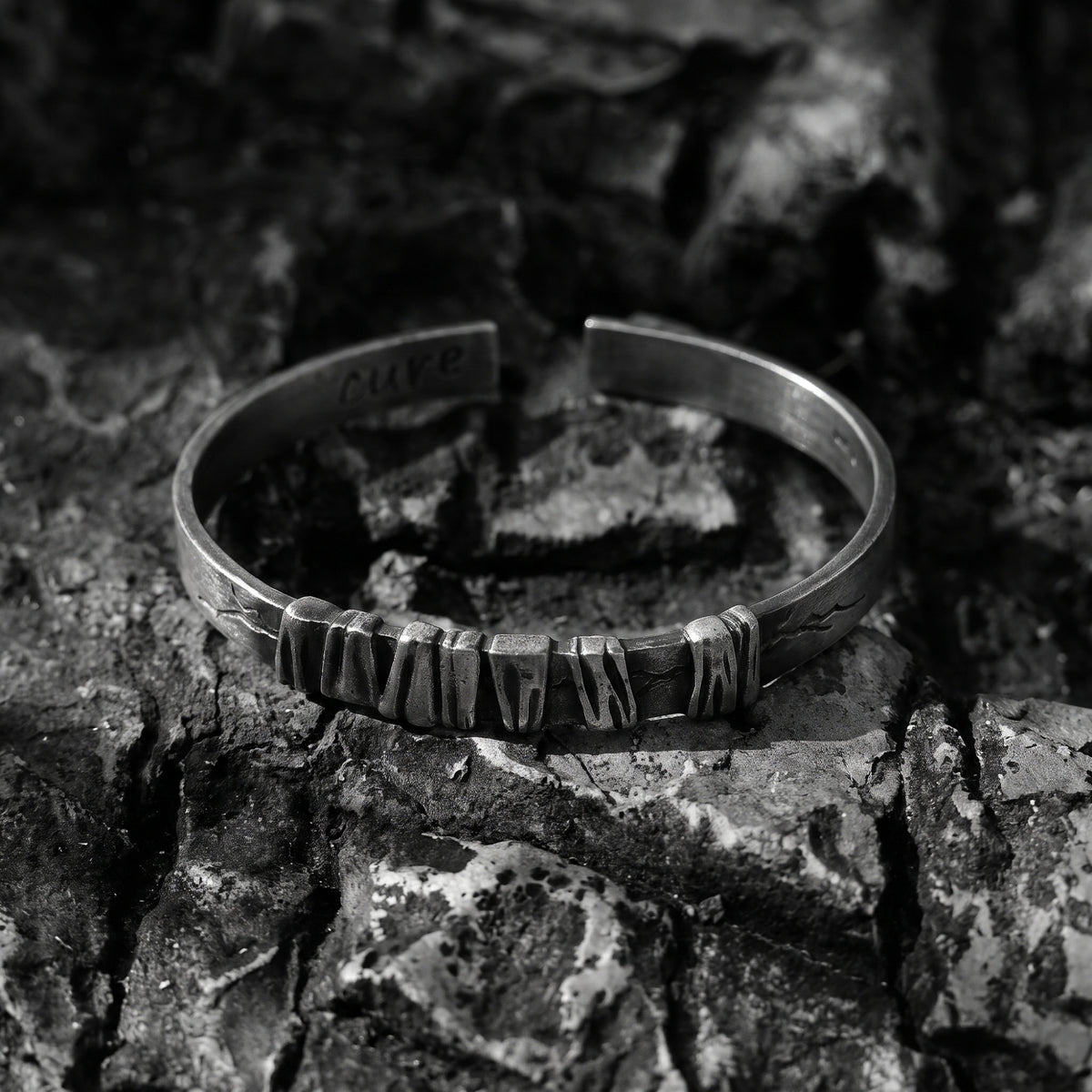 Front view of the silver open cuff bracelet with textured center segments, set on rough dark stone.