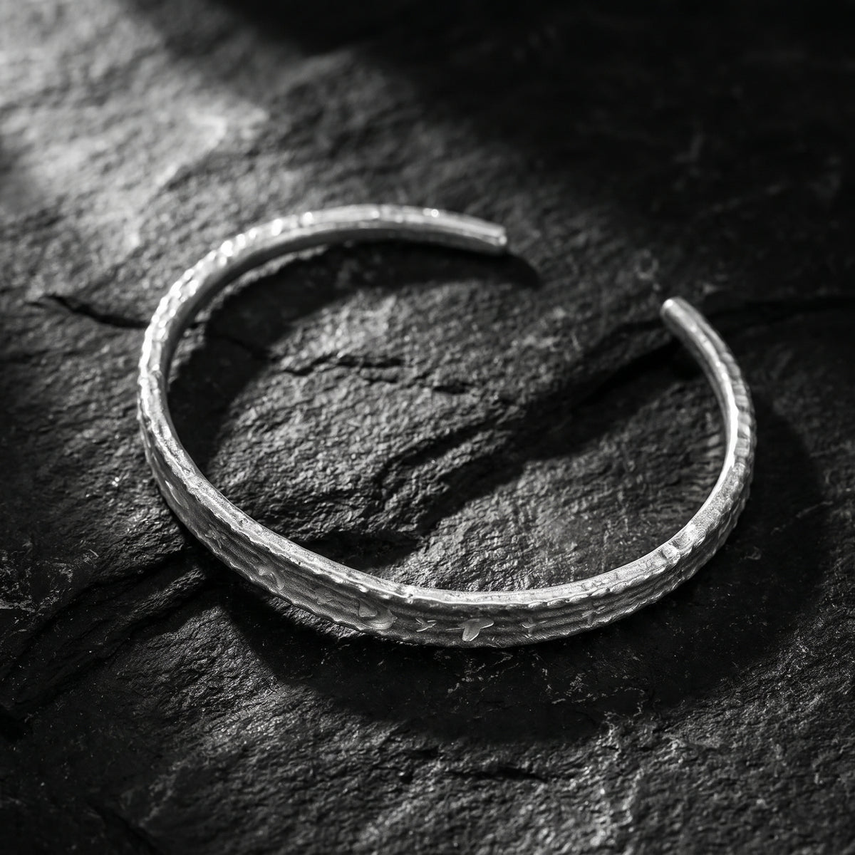 Angled overhead view of the open silver cuff bracelet with etched motifs on dark slate.