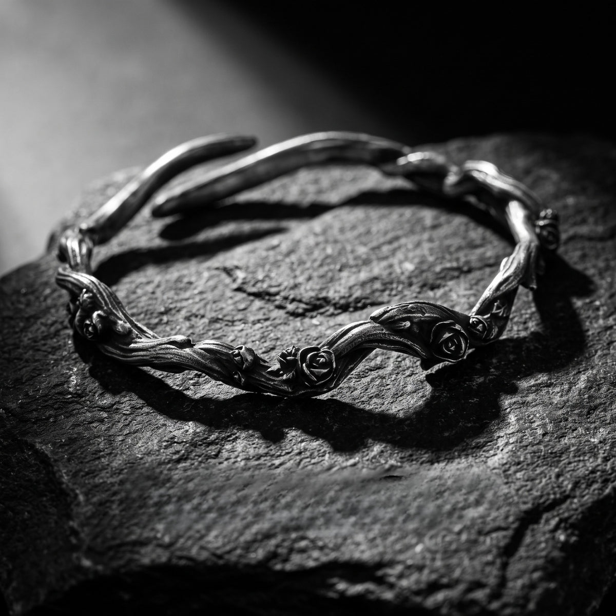 Low-angle view of a silver rose vine cuff bracelet resting on textured dark slate.