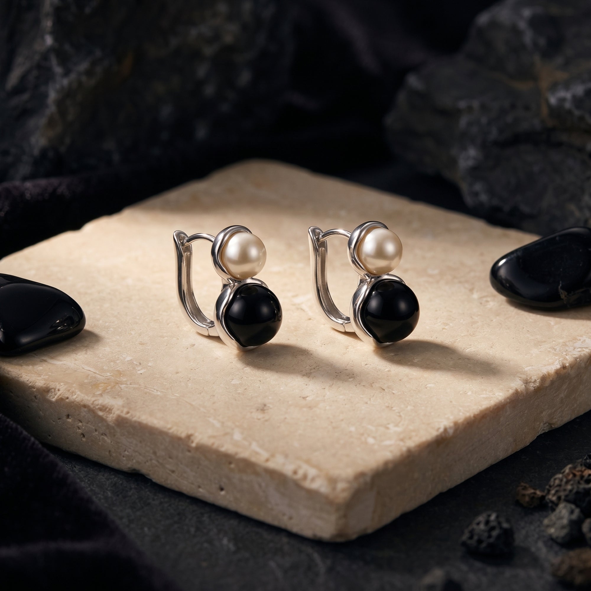 Side view of silver pearl and black onyx drop earrings on a textured stone with volcanic rock accents.