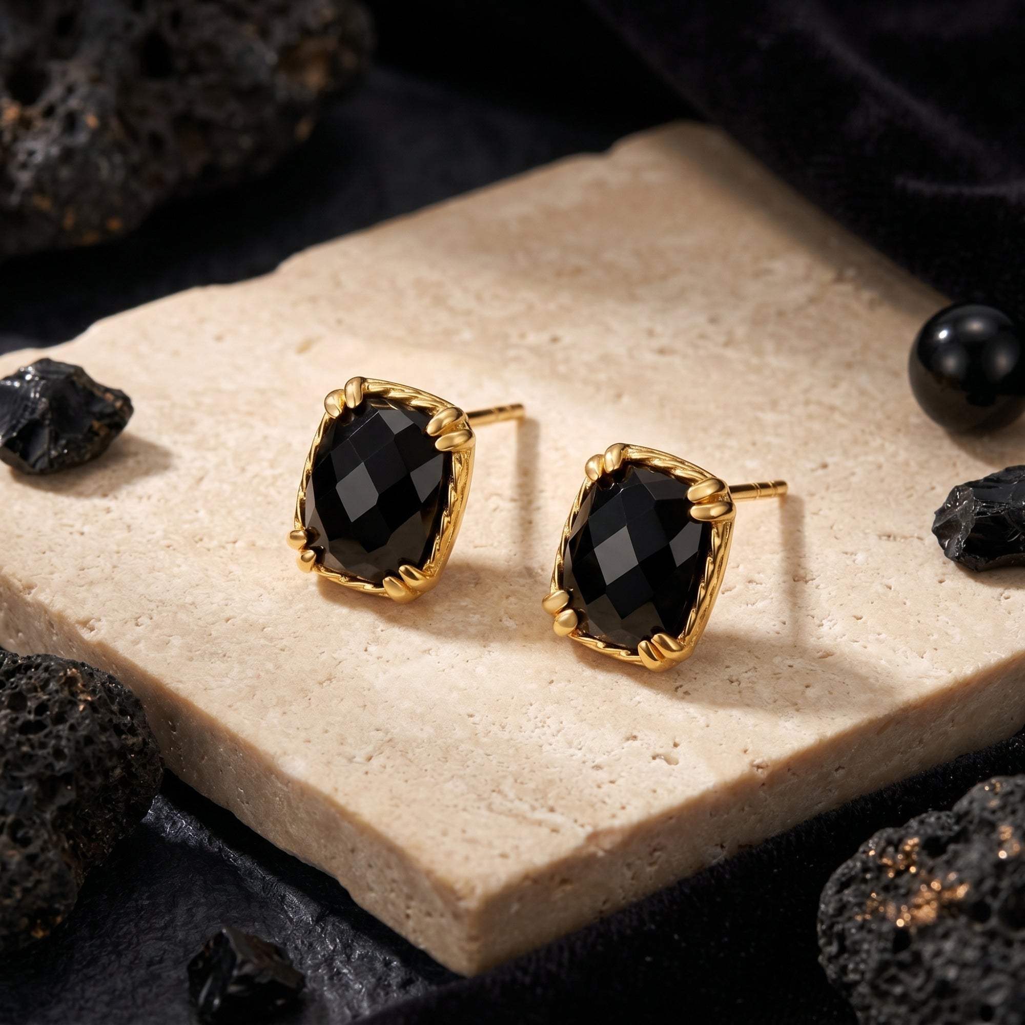 Gold square-cut black onyx stud earrings showing the faceted stone and textured prong setting on a stone base.