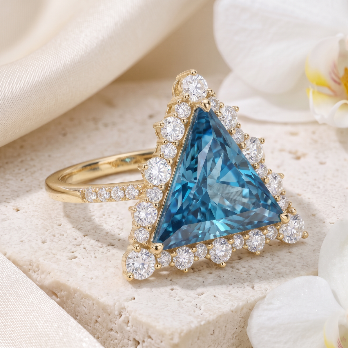 Side angle view of a trillion cut blue moissanite halo ring in yellow gold on a stone surface.