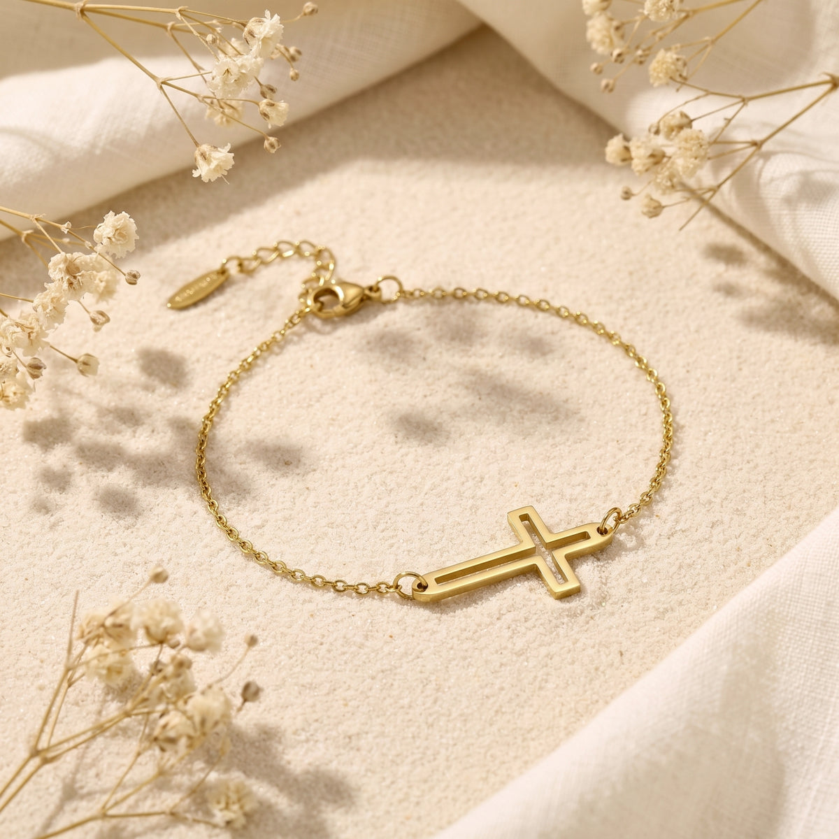 Full gold cutout cross chain bracelet laid flat on textured sand with its clasp and extender chain visible.