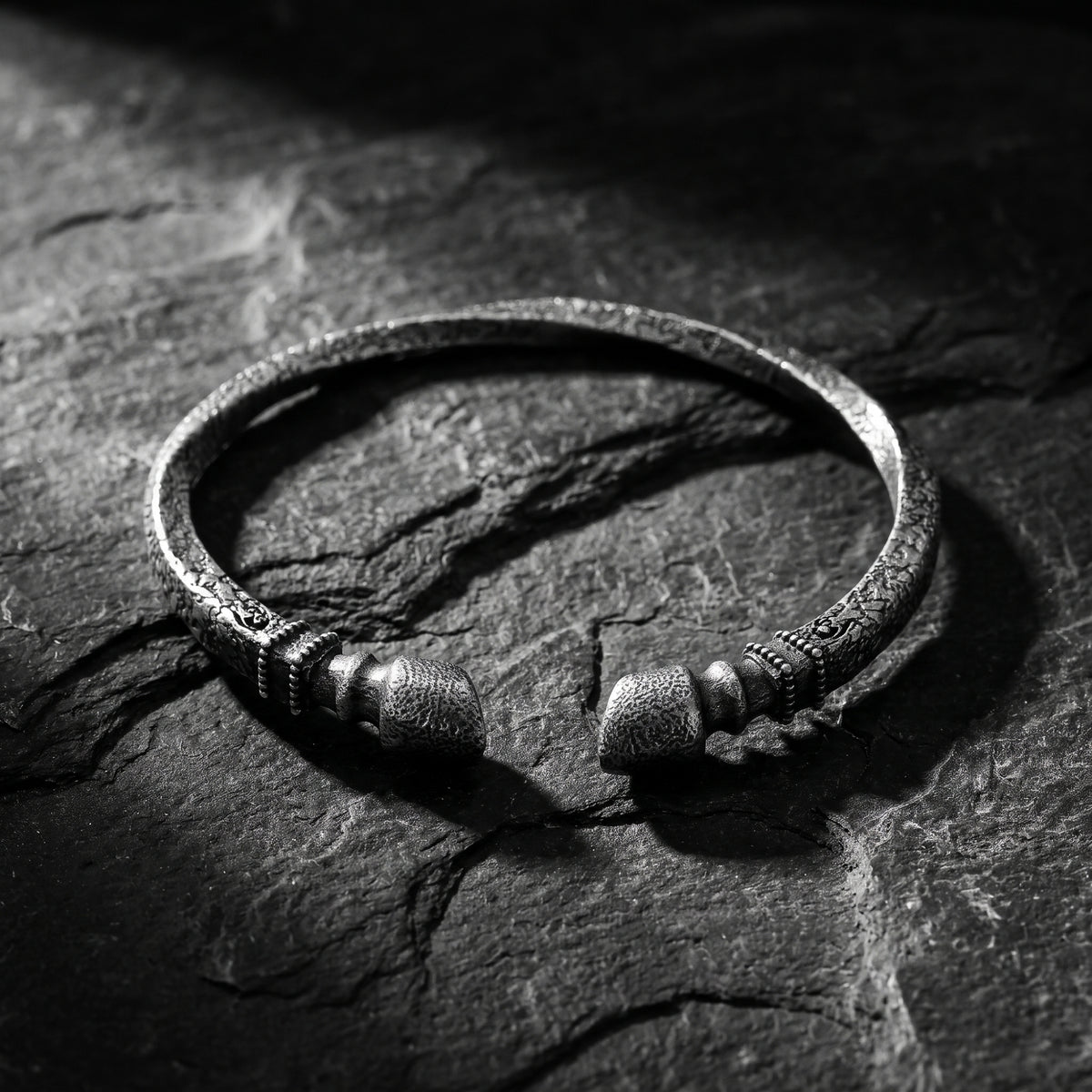 Frontal close-up of an open oxidized silver finial cuff bracelet resting on dark slate.