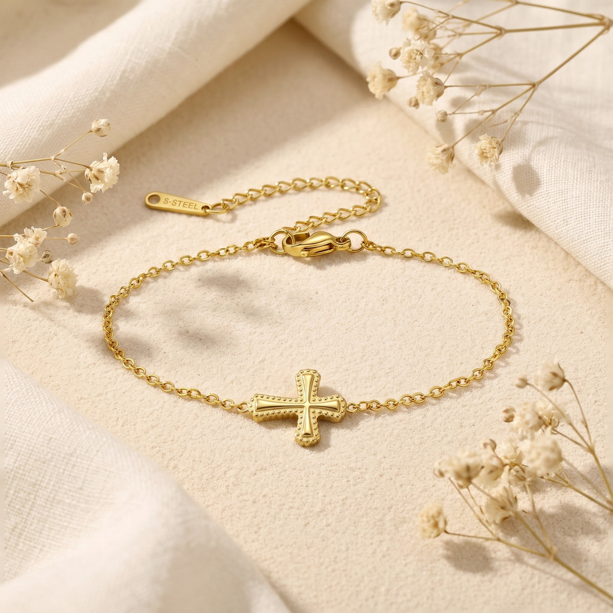Gold-toned cross bracelet shown flat with a beaded-edge charm, clasp, extender chain, and S-STEEL tag.