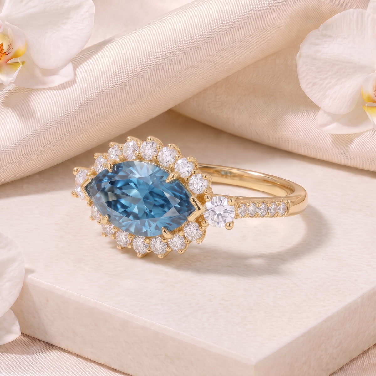 Side angle view of a yellow gold marquise blue moissanite halo ring with diamond accents on a display pedestal.
