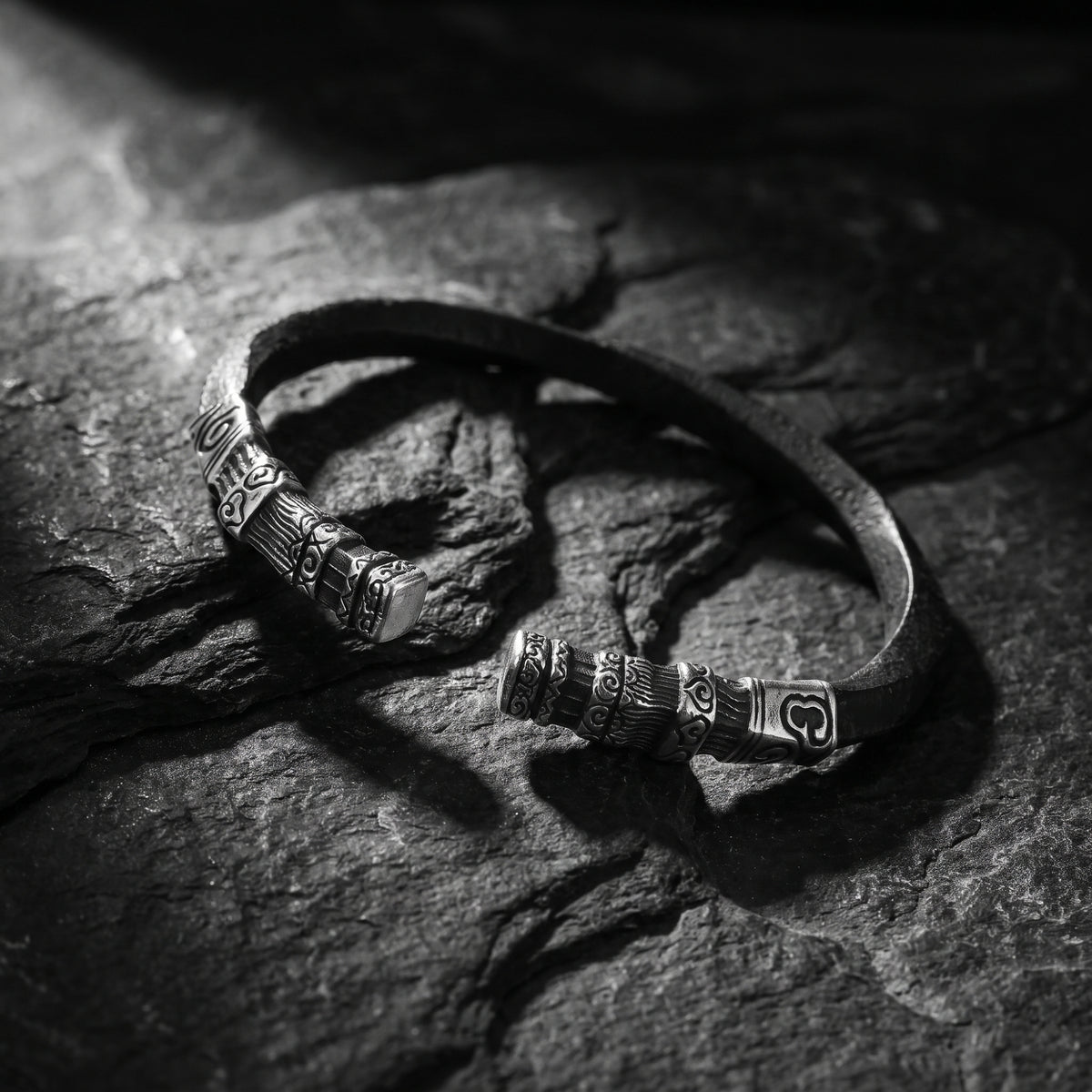 Angled close view of the carved silver open cuff bracelet with patterned ends on textured slate.