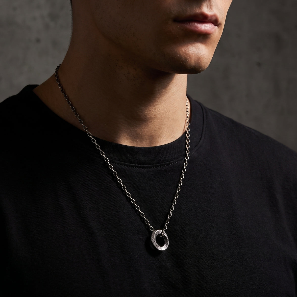 Three-quarter view of a model wearing the textured silver circle pendant necklace over a black shirt.
