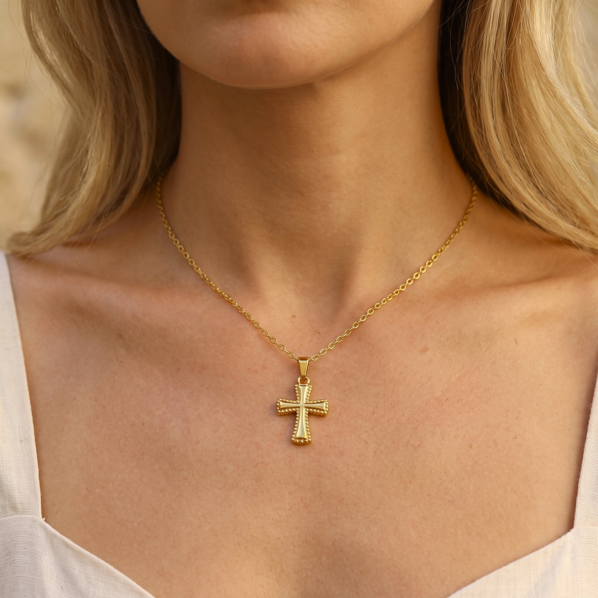 Front view of a woman wearing the gold-tone beaded cross necklace paired with a light-colored top.