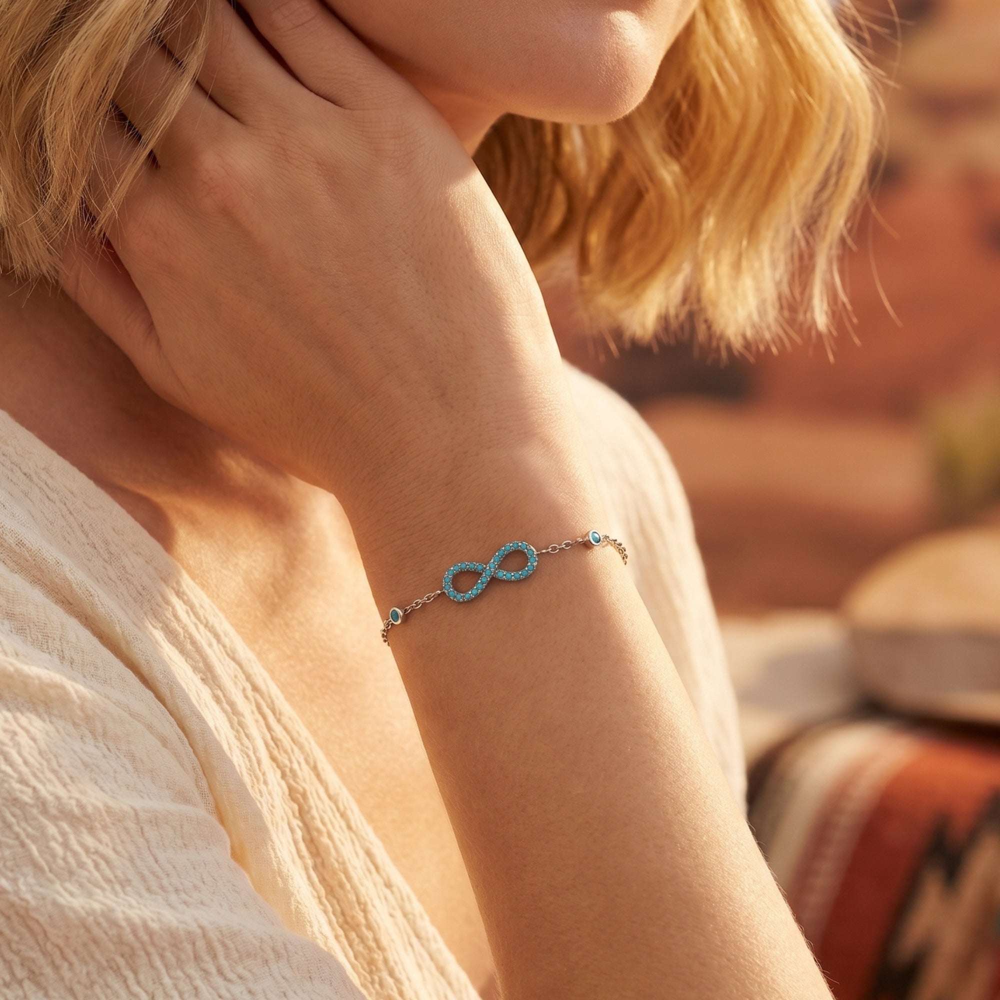Dainty silver chain bracelet with turquoise infinity charm and bezel-set beads on a wrist.