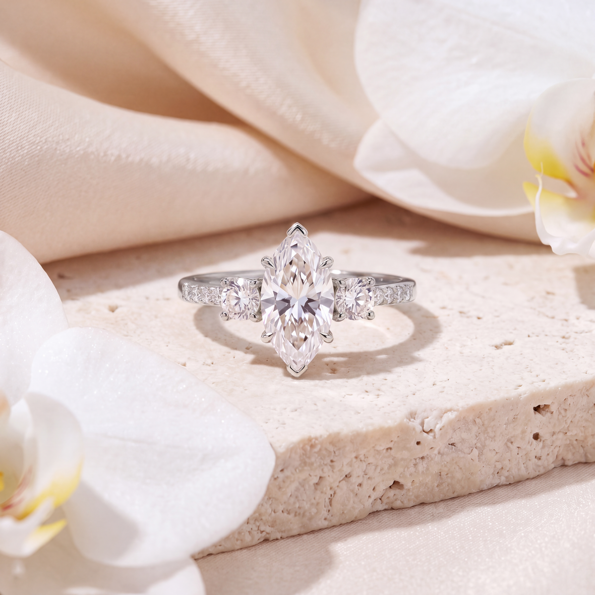 Front view of a white gold marquise cut moissanite three-stone ring on a stone surface.