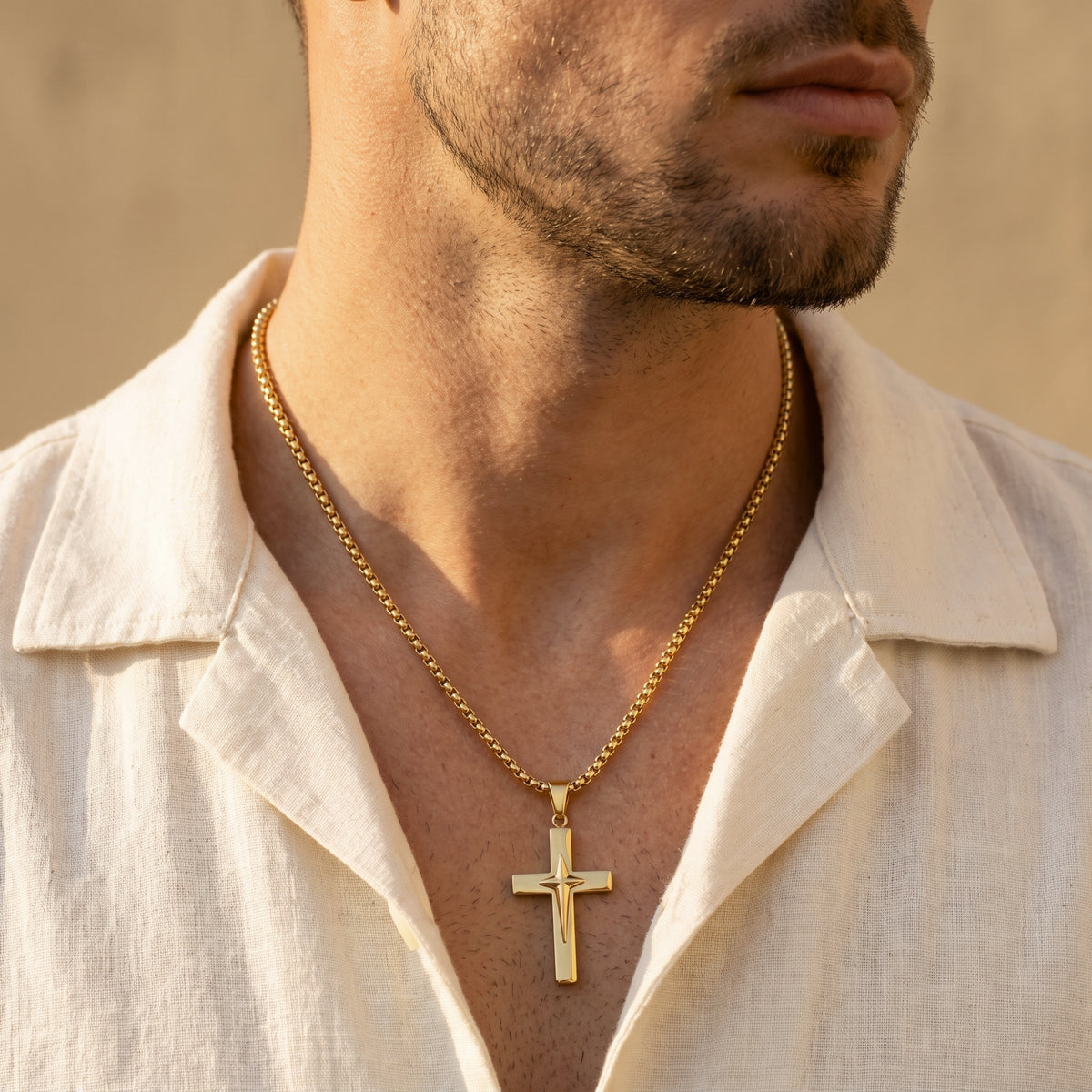 Gold-tone star cross necklace worn against a man's chest with an open cream shirt in warm light.