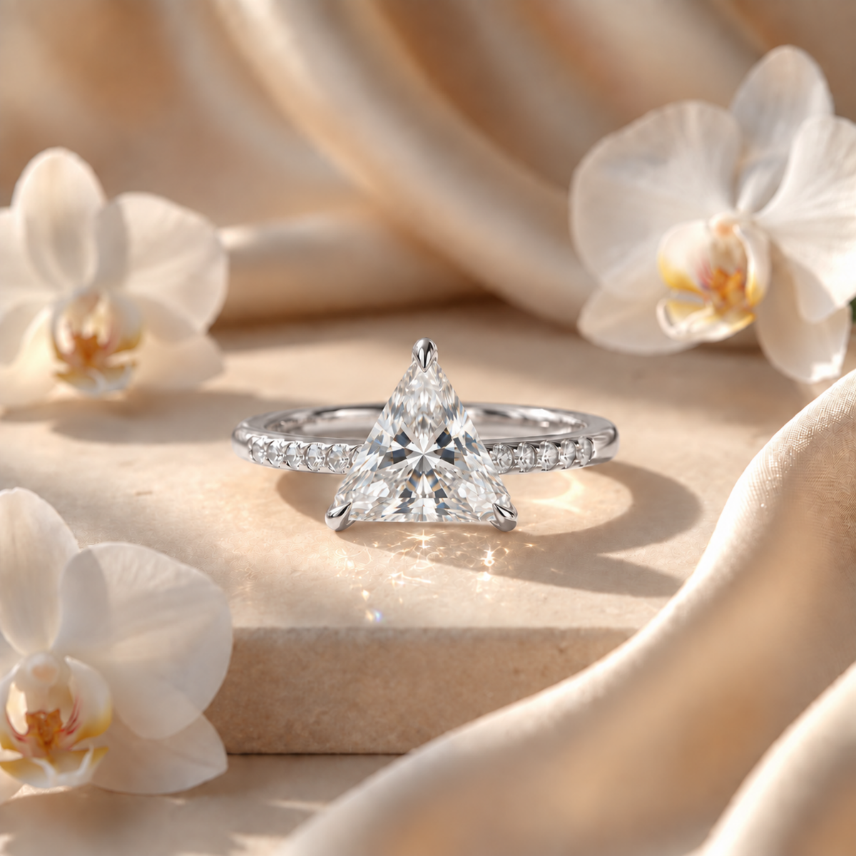 White gold triangle-cut moissanite ring with a pavé band shown on a beige backdrop.
