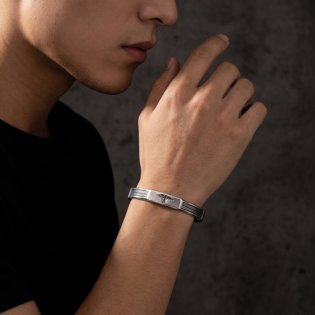 Side-profile view of a man wearing the silver raven cuff bracelet with his hand near his chin.