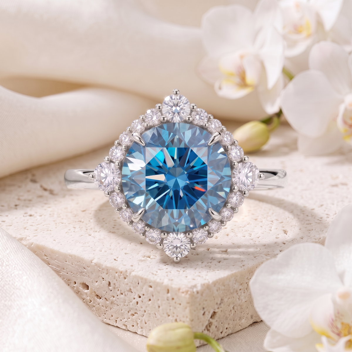A white gold halo ring featuring a round blue moissanite centerpiece on a textured stone surface.