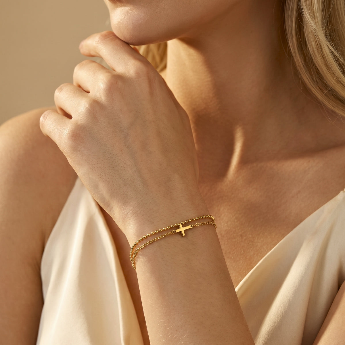 Woman wearing a gold-finish double-chain cross bracelet with her hand resting near her chin.