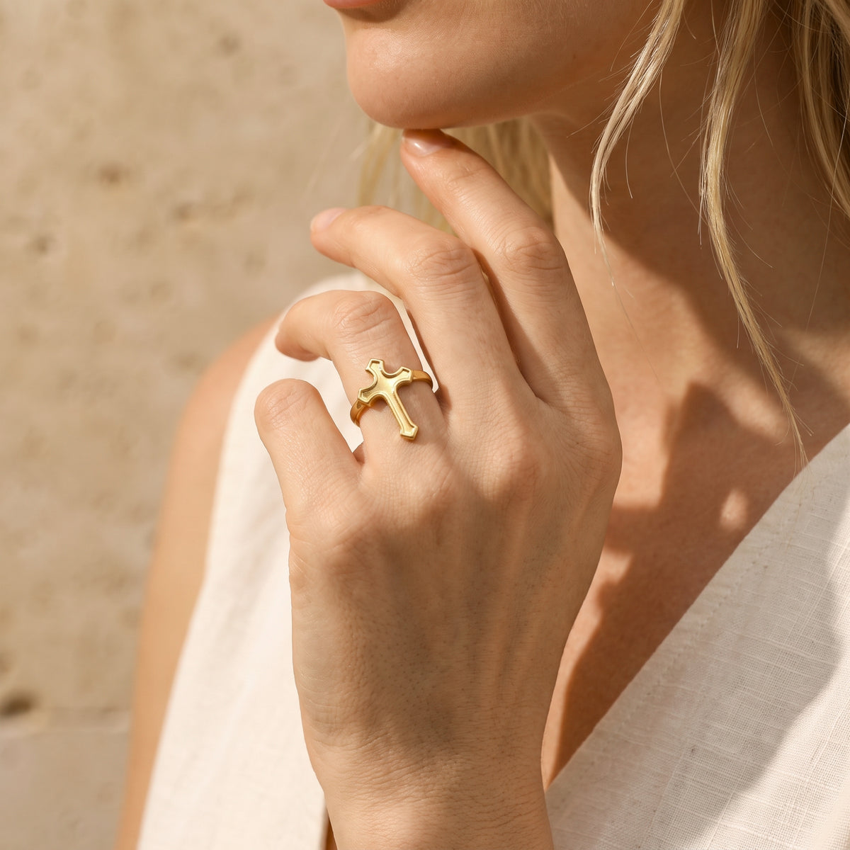 Gold-tone cross ring worn on a woman's finger in a sunlit medium lifestyle portrait near her face.