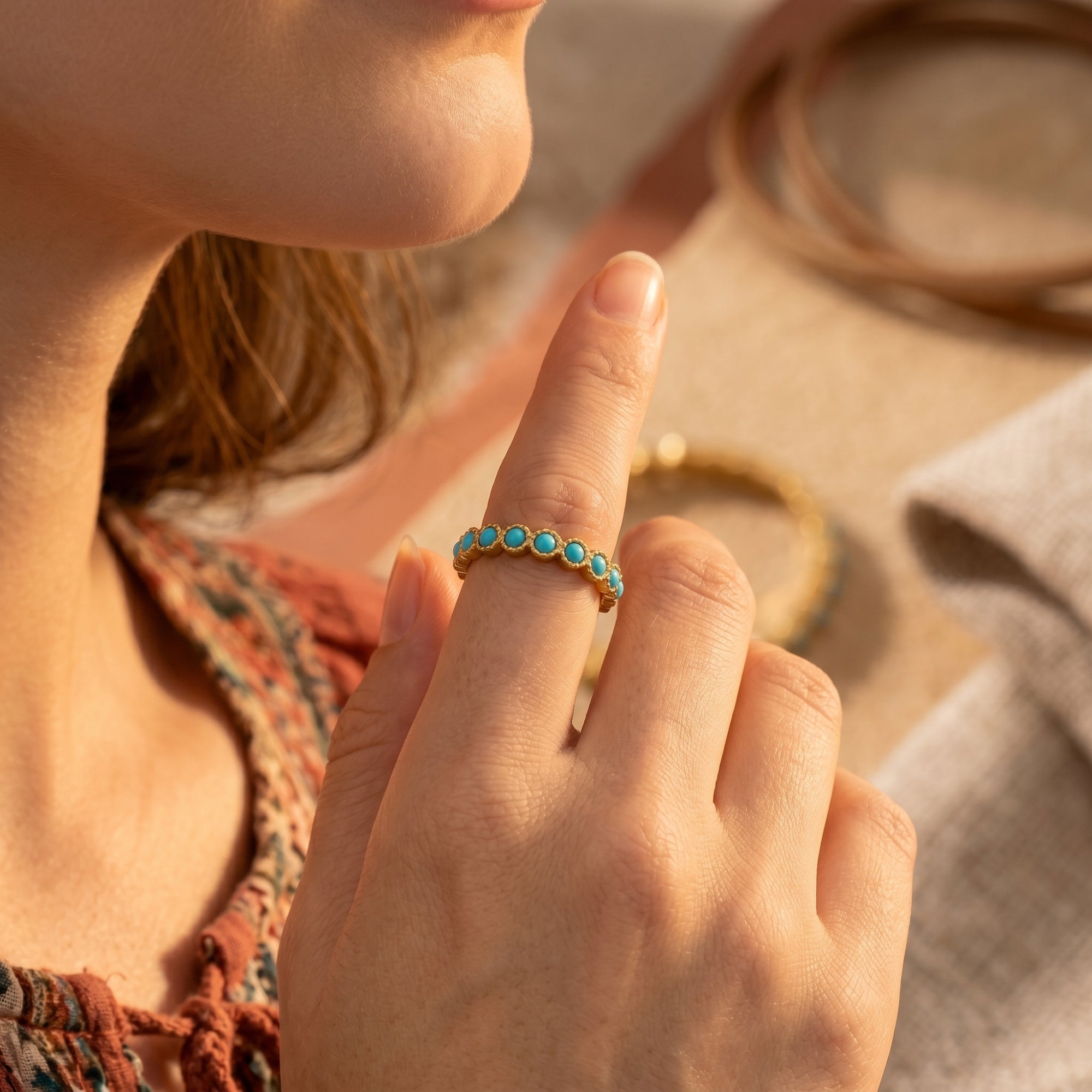 Close-up of the gold Zia turquoise eternity ring on a finger, showing the hand-set round blue stones.