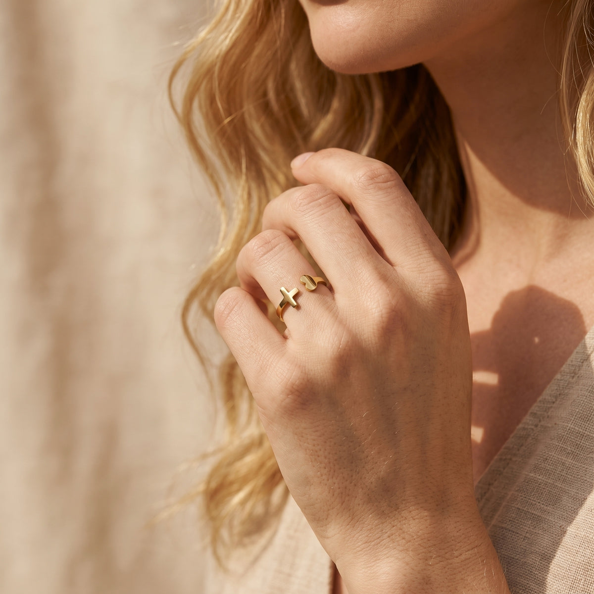 Close-up of a woman wearing the gold-tone heart and cross open ring on her ring finger beside her shoulder.