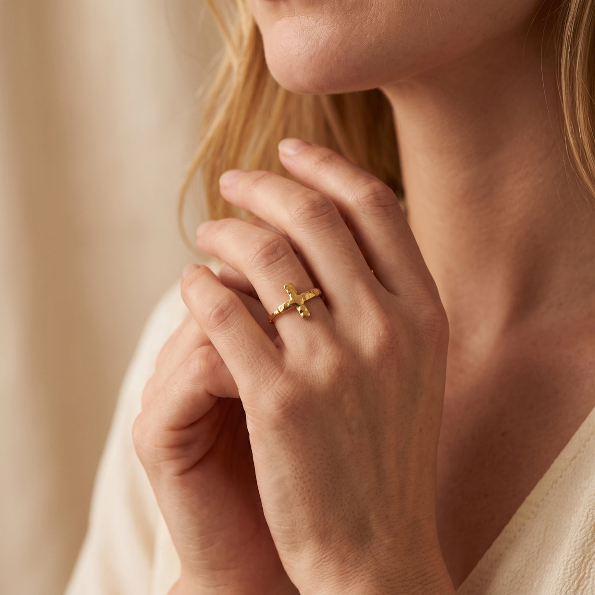 Gold-tone hammered cross ring worn on a finger as the model holds her hands near her neck.