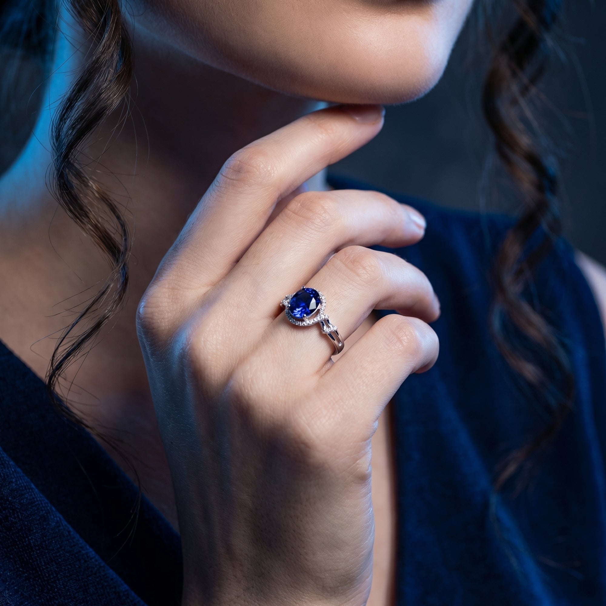 Side view of the 18K white gold oval tanzanite halo ring worn on a model's hand.