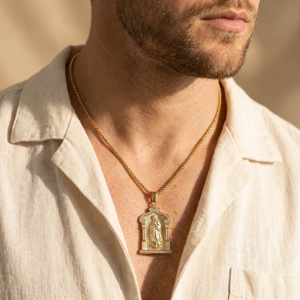 Chest-up view of a man wearing the gold-tone Guadalupe arch pendant over an open white shirt.