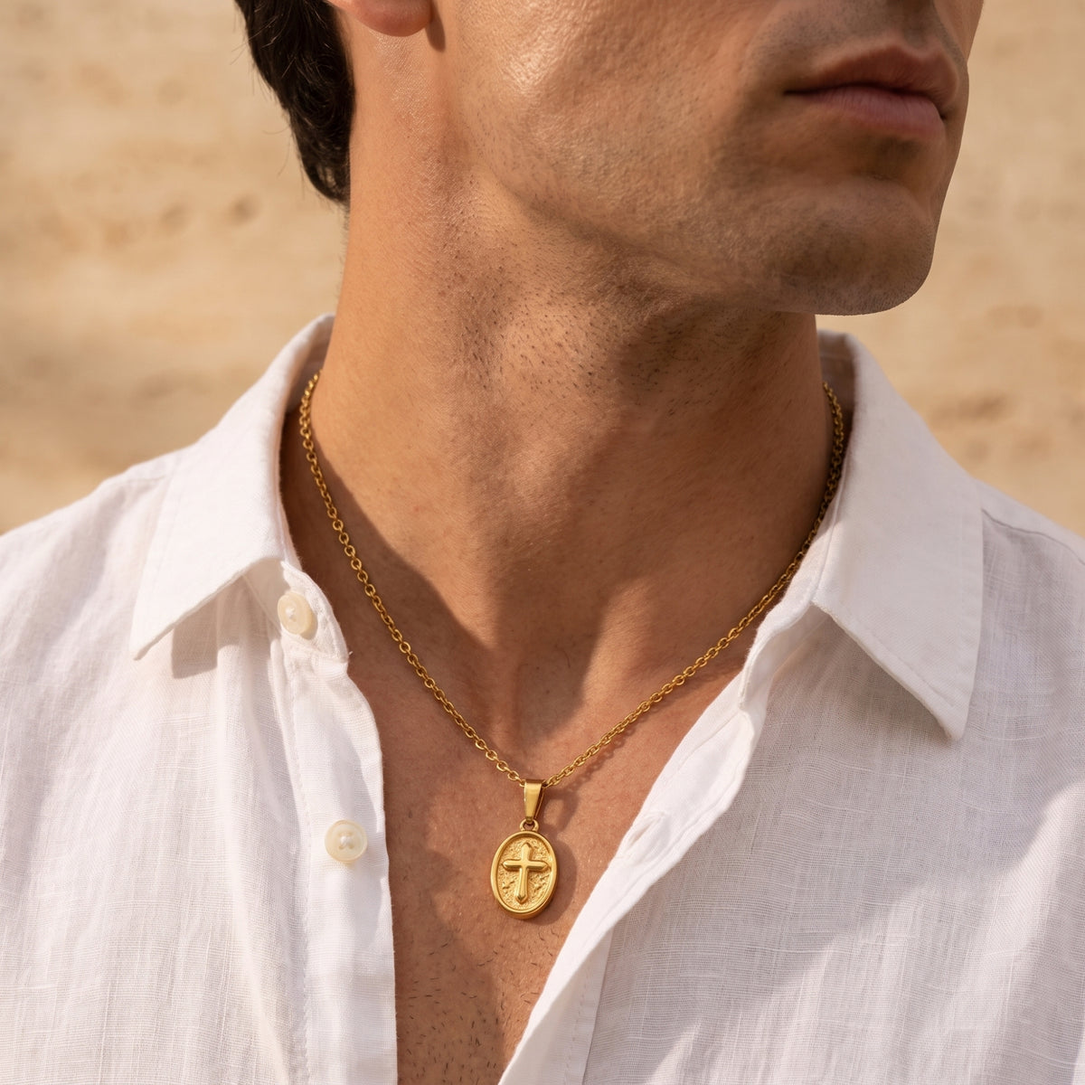 Man wearing a gold-tone oval cross medallion necklace with an open white shirt.