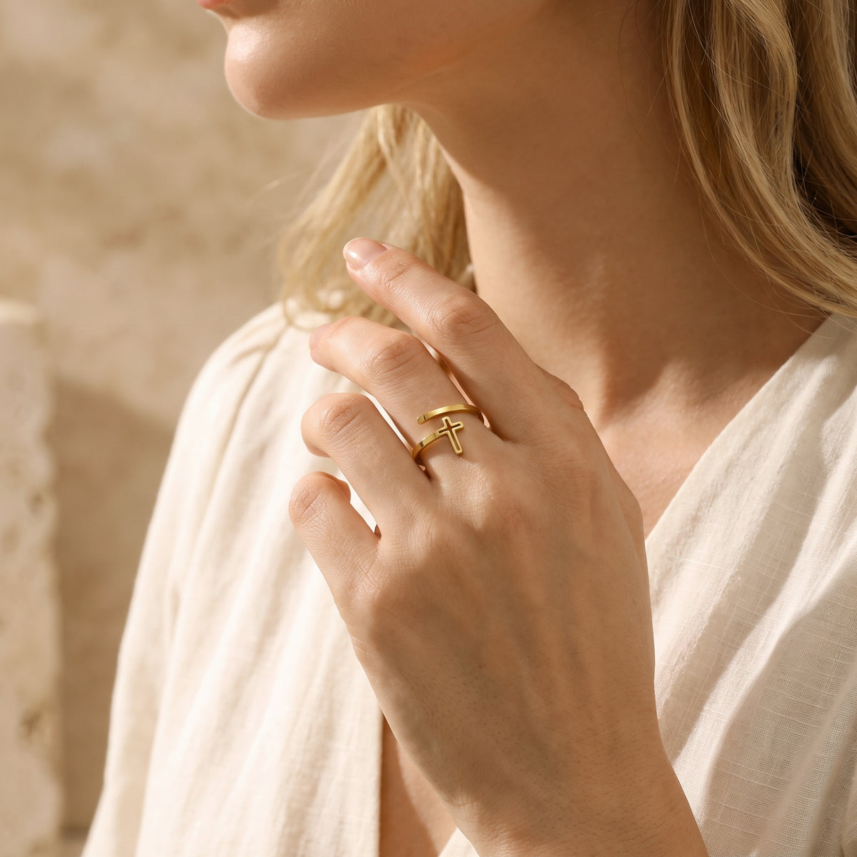 Person wearing the gold-finish open-wrap cross ring against a cream-colored top.