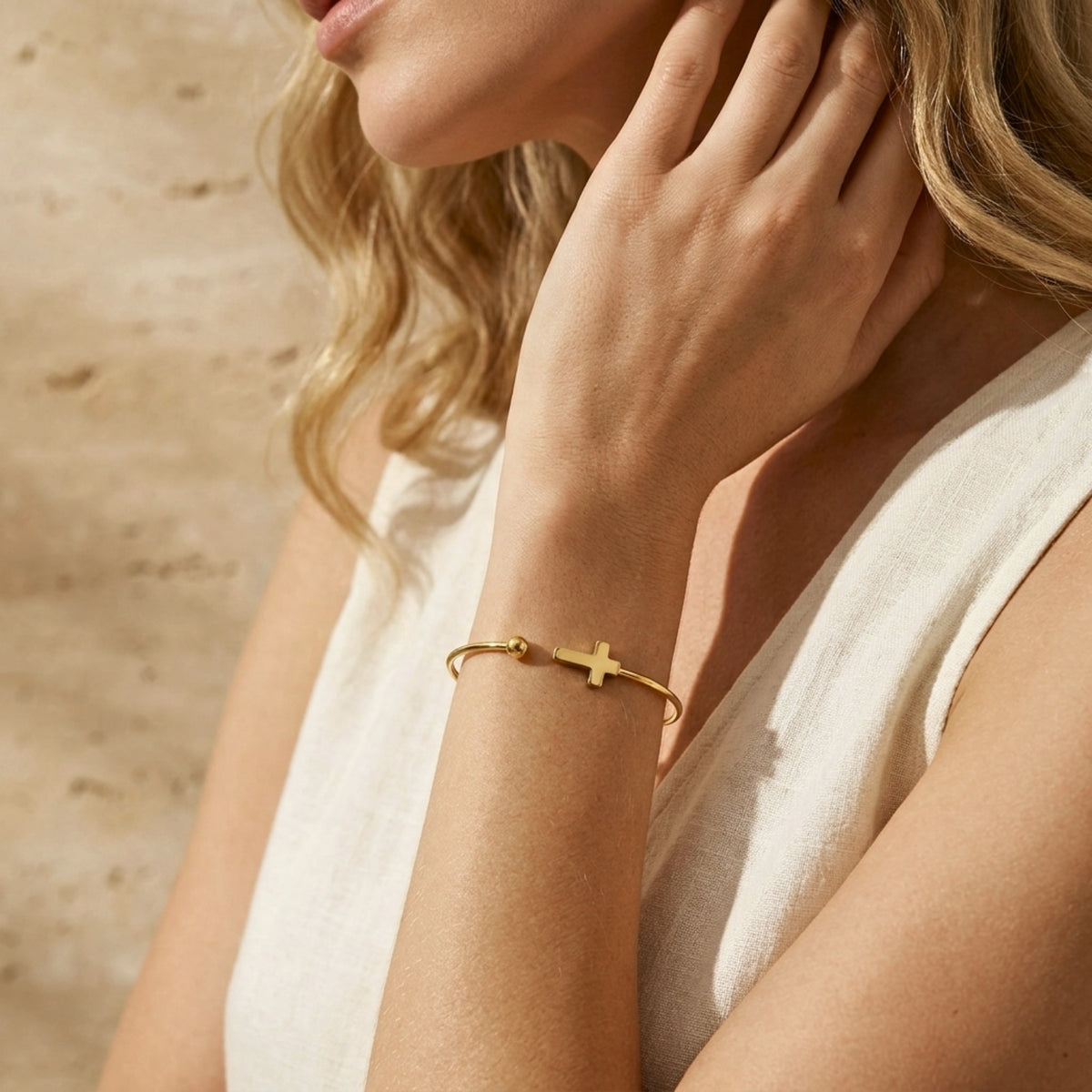 Woman wearing the gold-tone cross cuff bracelet on her wrist, styled with a cream sleeveless top.