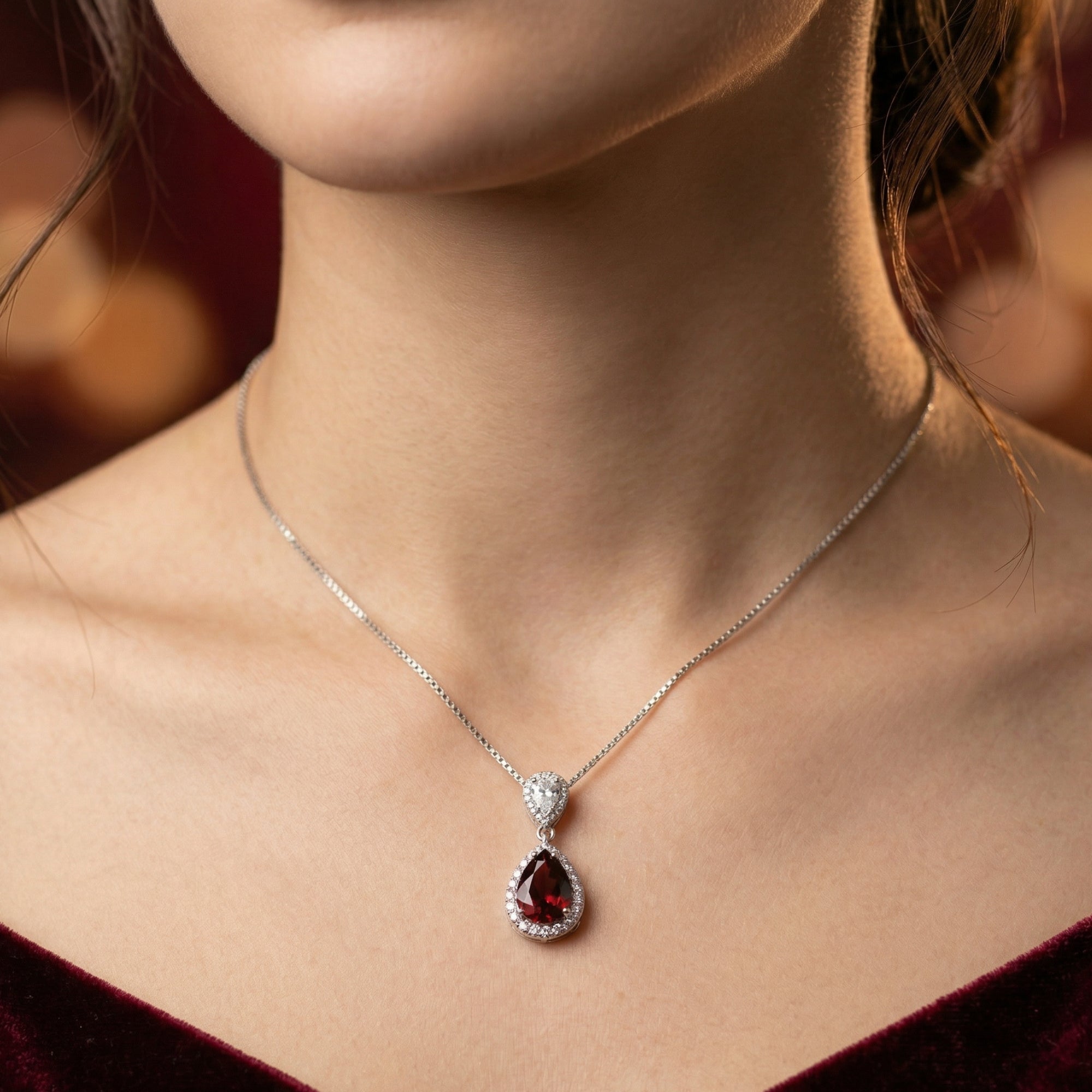 Frontal view of the Ilaria pear cut garnet necklace in silver worn by a model against a dark red dress.