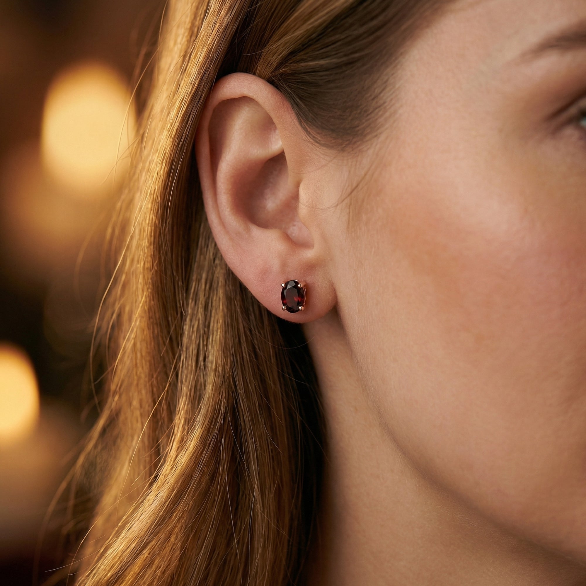 Side profile of a woman wearing an 18K rose gold oval garnet stud earring.