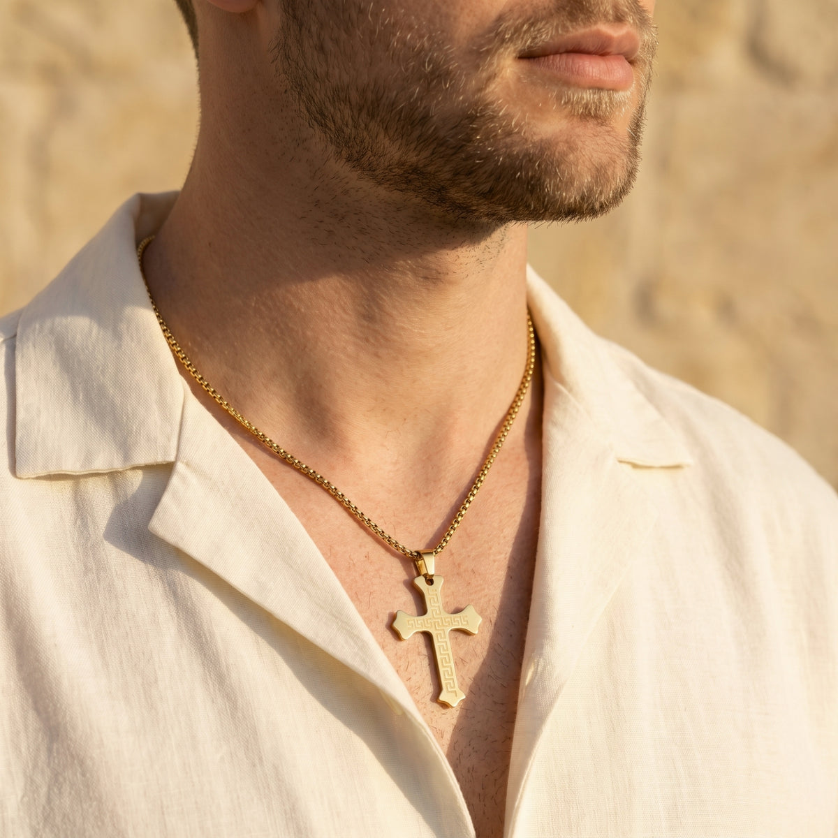 Close-up of a man wearing the gold-toned Greek key cross necklace in a three-quarter view.