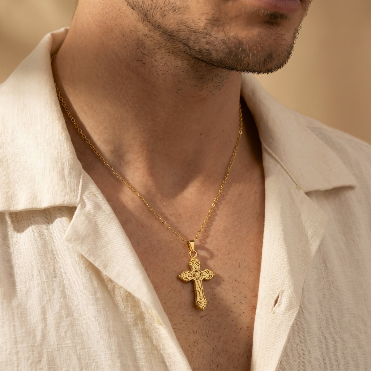 Man wearing a gold-tone ornate cross necklace with an open white shirt.