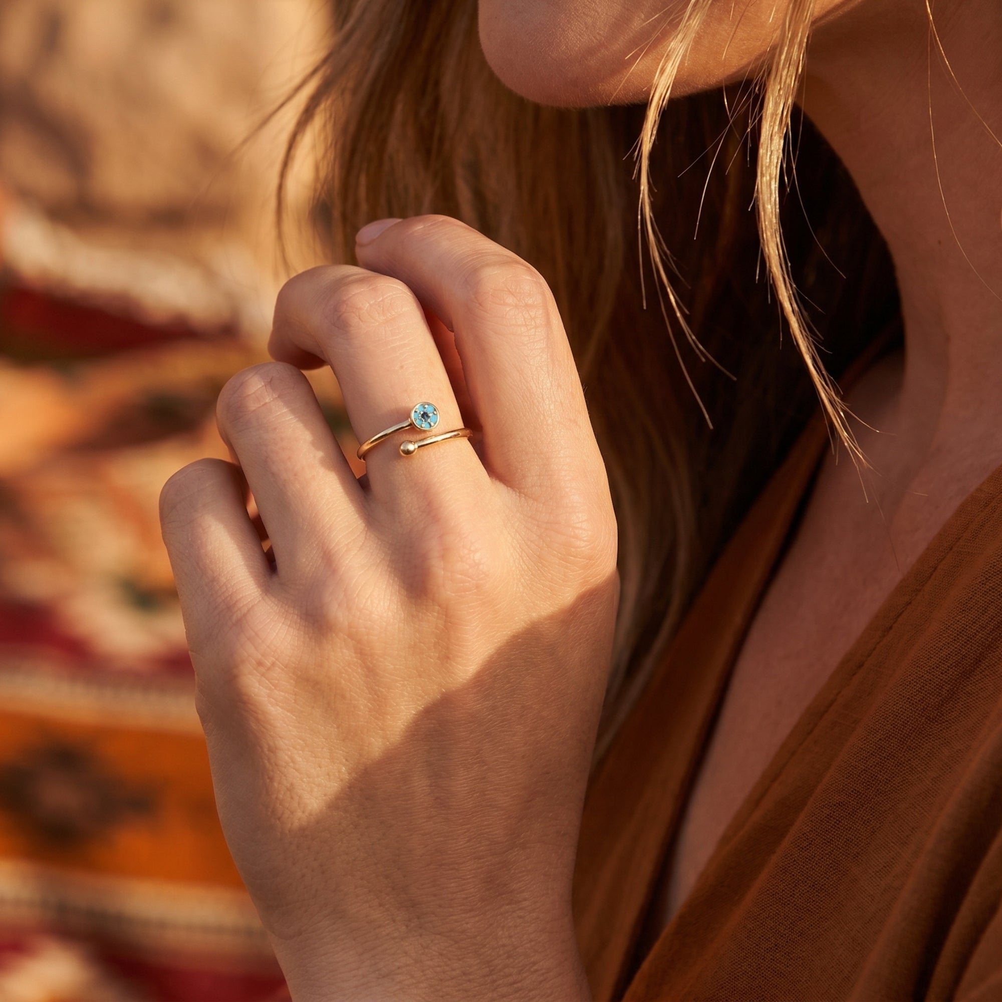 Close-up of a woman's hand wearing the gold Cibola turquoise bypass ring against a desert background.