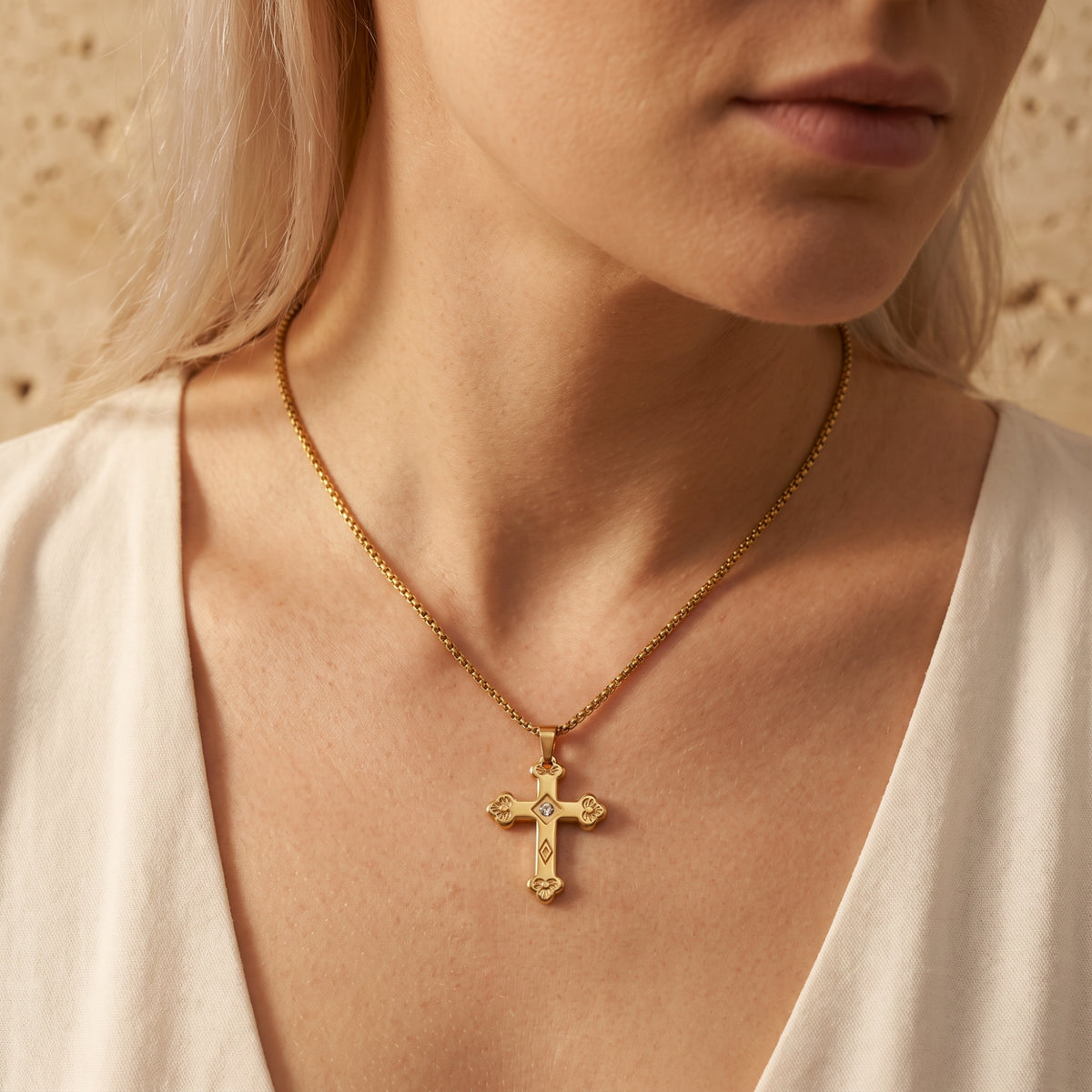 Close-up of the gold-tone floriated cross pendant centered on a model wearing a cream open-neck top.
