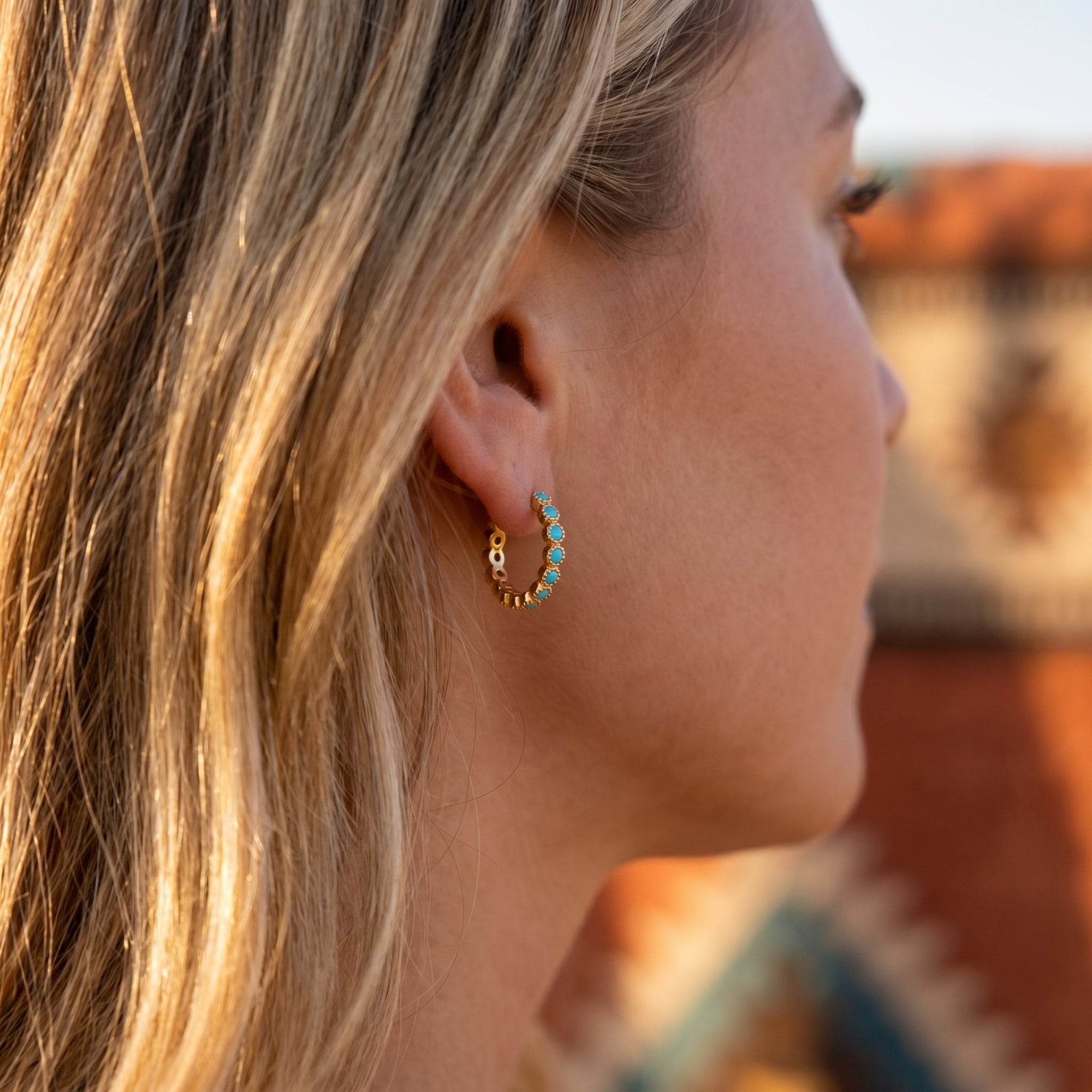 Profile view of a model wearing gold vermeil huggie earrings with round turquoise cabochon stones.