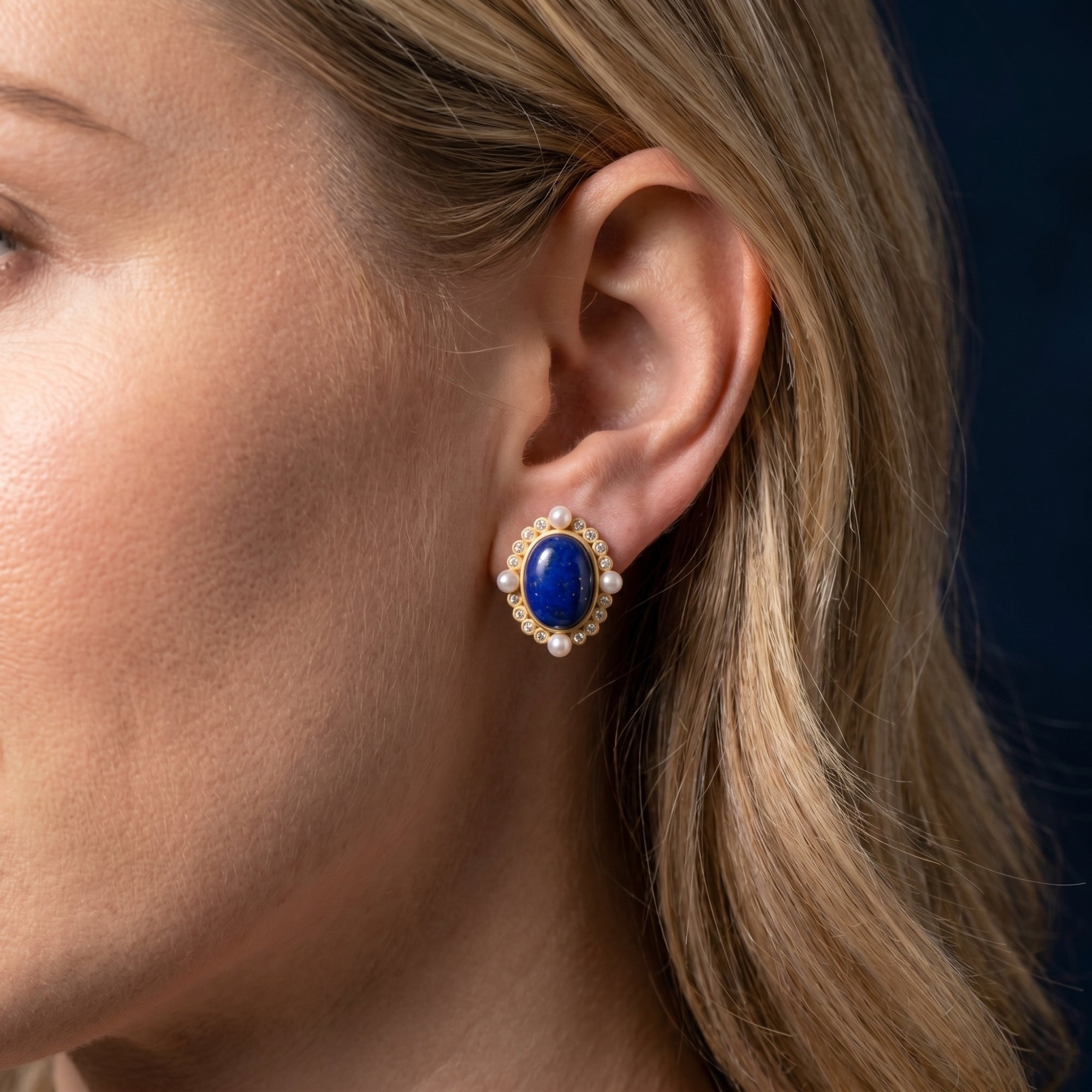 Profile view of a model wearing a gold-plated oval lapis lazuli stud earring with pearl and crystal accents.