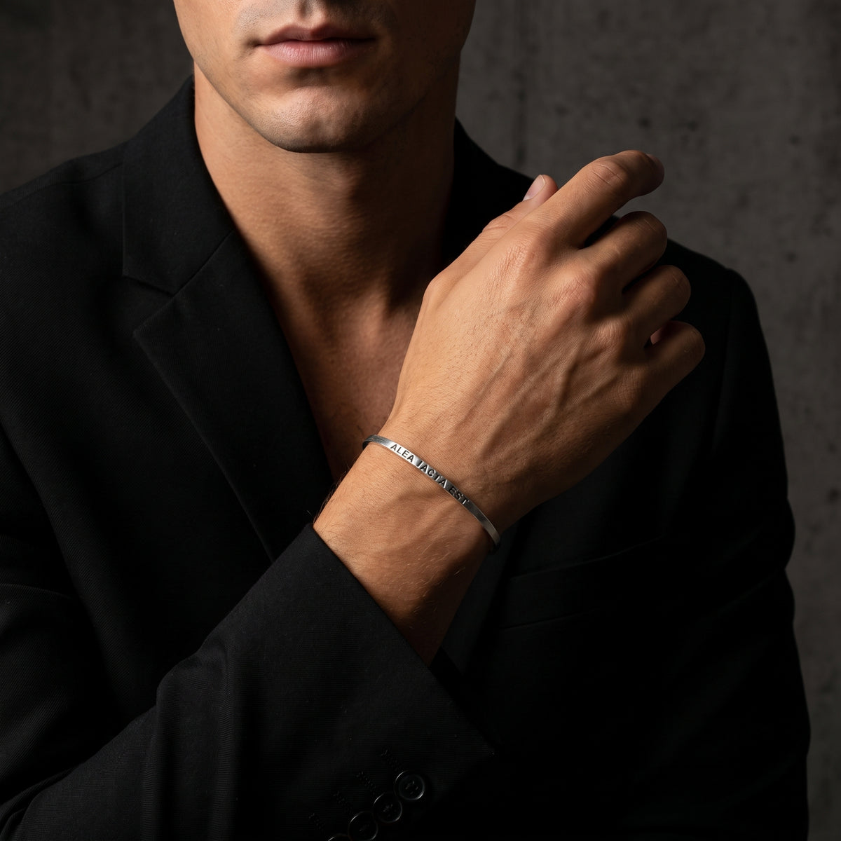 Man wearing the engraved silver cuff bracelet on his wrist, shown against a black blazer.