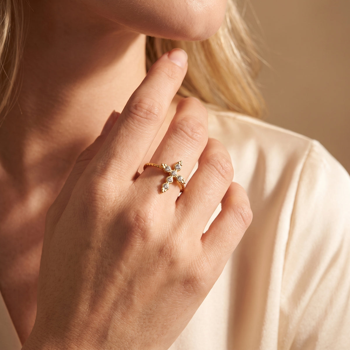 Model wearing the gold-tone crystal cross ring on her ring finger near her neck, shown from an angled view.