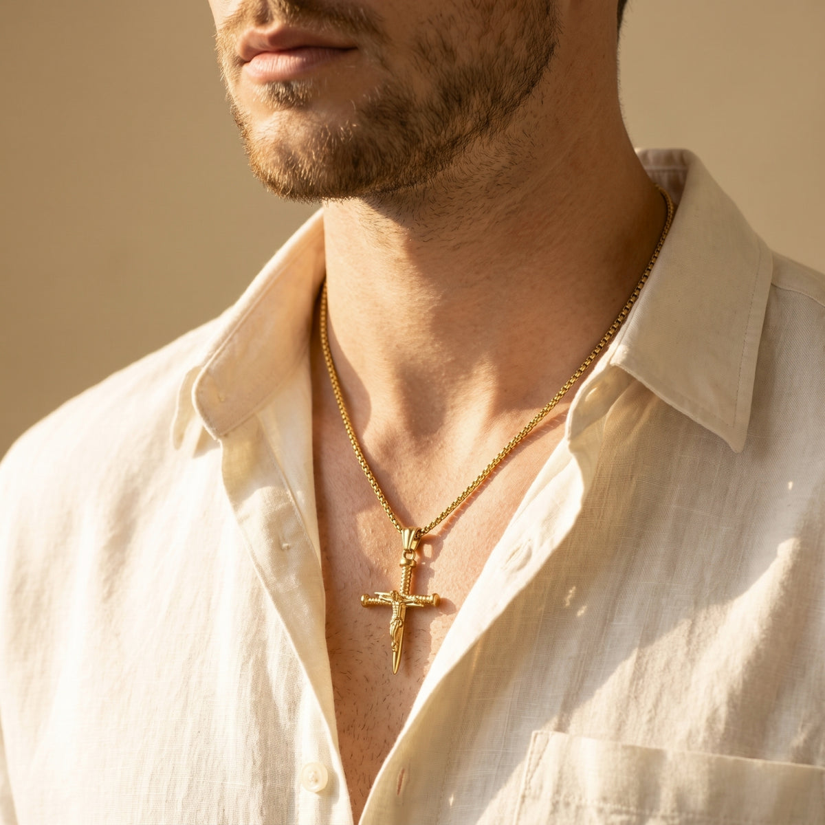 Gold-tone nail cross necklace worn on a man in warm sunlight with an open white shirt.