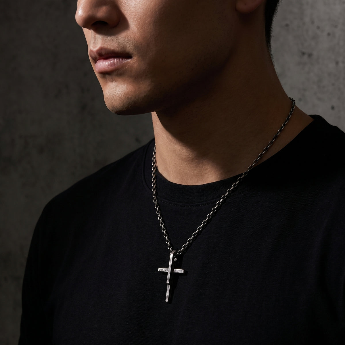 Three-quarter view of a man wearing the textured silver cross pendant necklace over a black shirt.