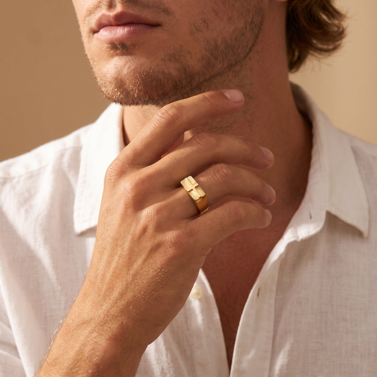 Man wearing the gold-tone cross signet ring on his ring finger, with his hand raised near his chin.