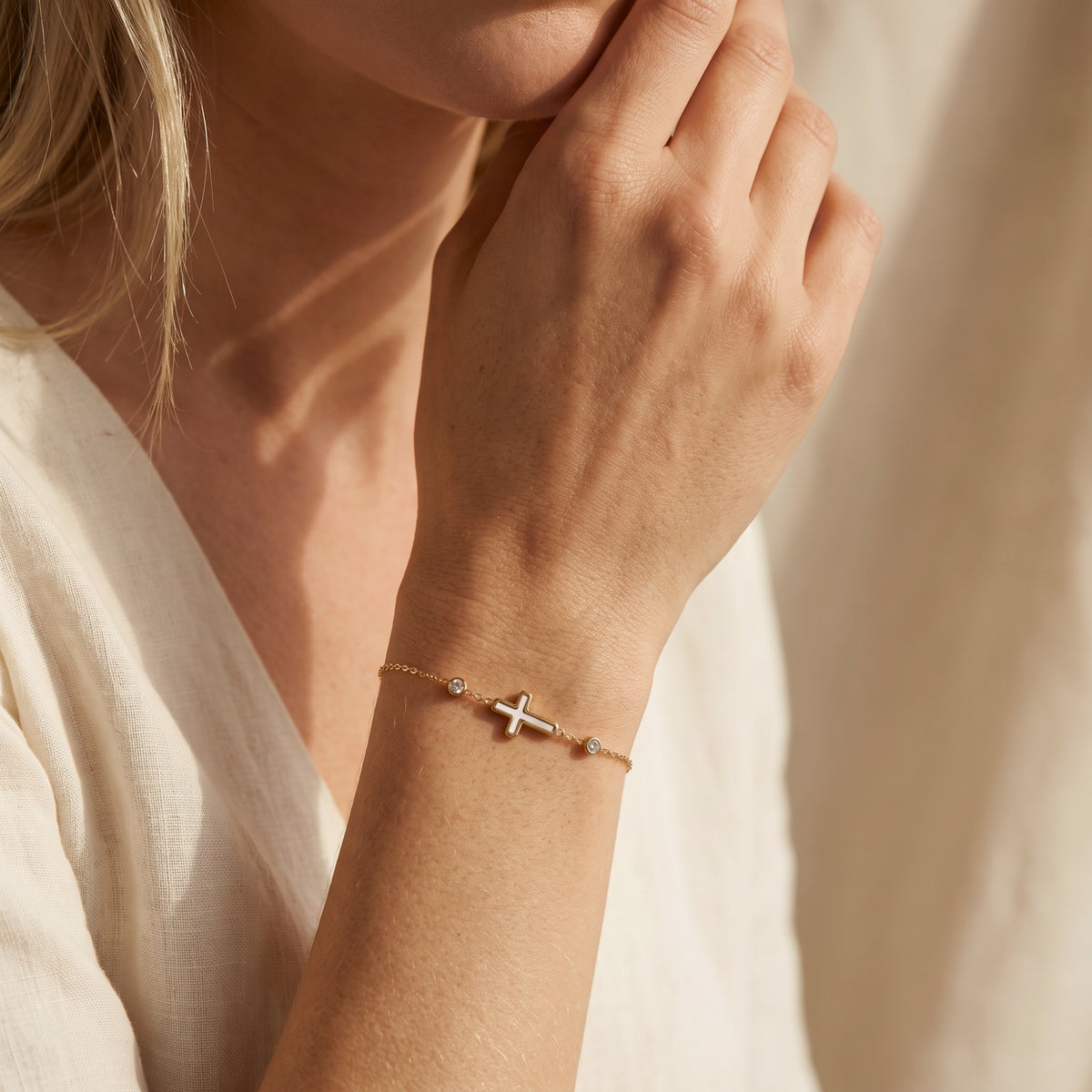 Person wearing the gold-tone bracelet with a white cross on the wrist, with a hand raised near the face.