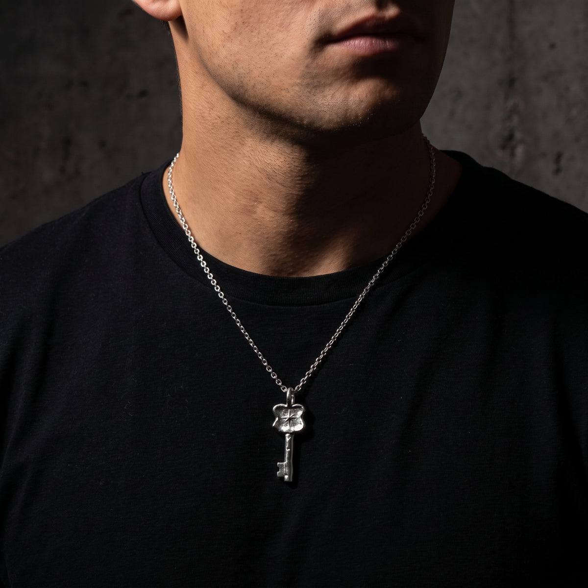 Front view of a man wearing a silver starburst key necklace centered over a black crewneck shirt.