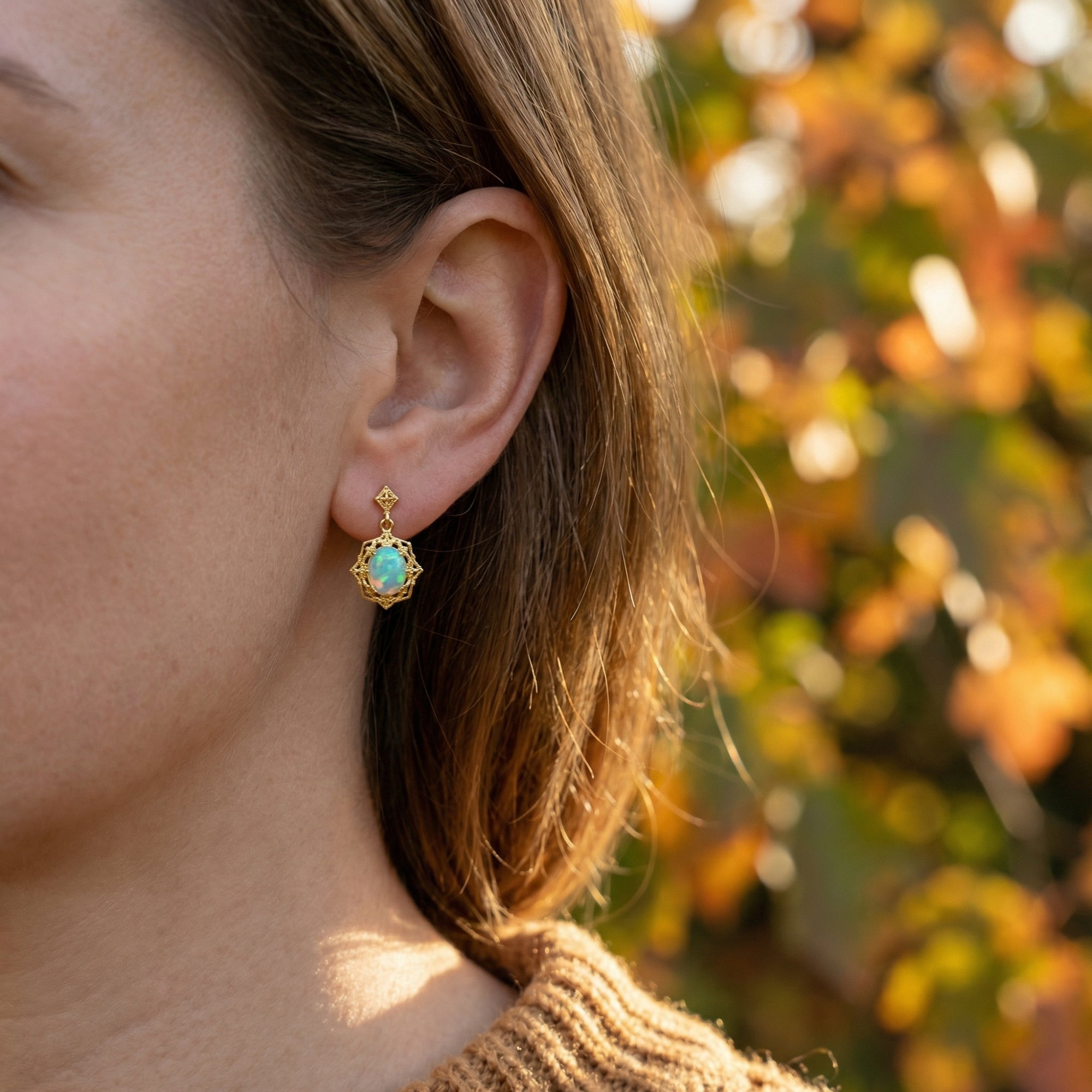 Side profile of a woman wearing a gold-tone S925 silver drop earring with a genuine oval white opal.