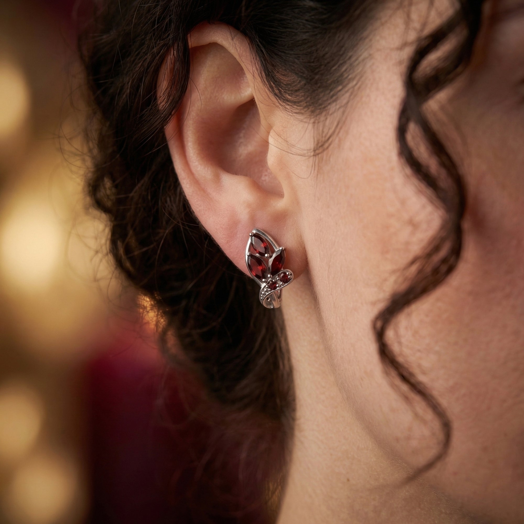 Close-up view of a natural garnet and silver drop earring worn on a model's ear.