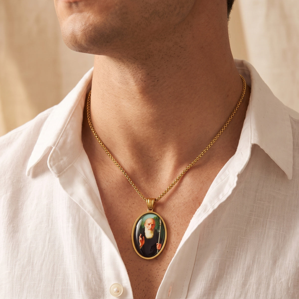 Gold-tone saint medallion necklace worn by a man with an open white shirt.