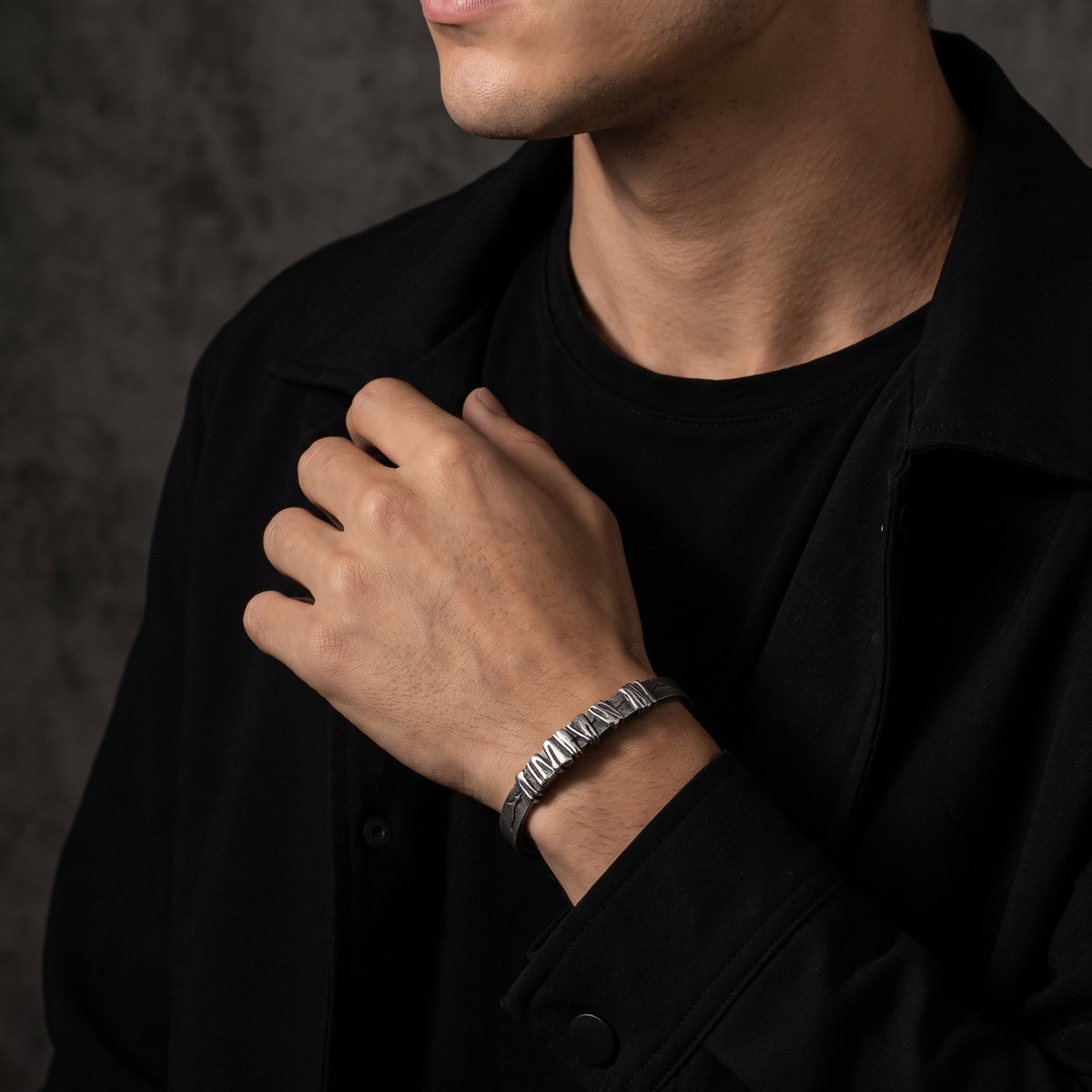 Man wearing the silver segmented cuff bracelet, with his hand resting against a black jacket.
